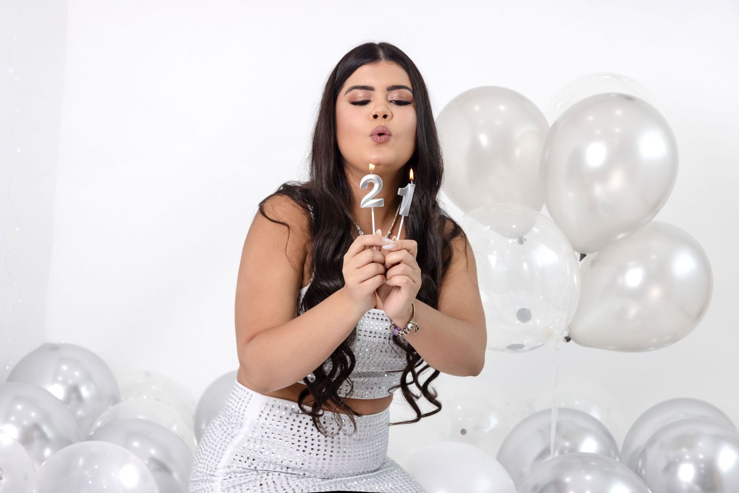 Someone wearing a white dress blows out party balloons while celebrating against a light background. Adult and kids birthday.