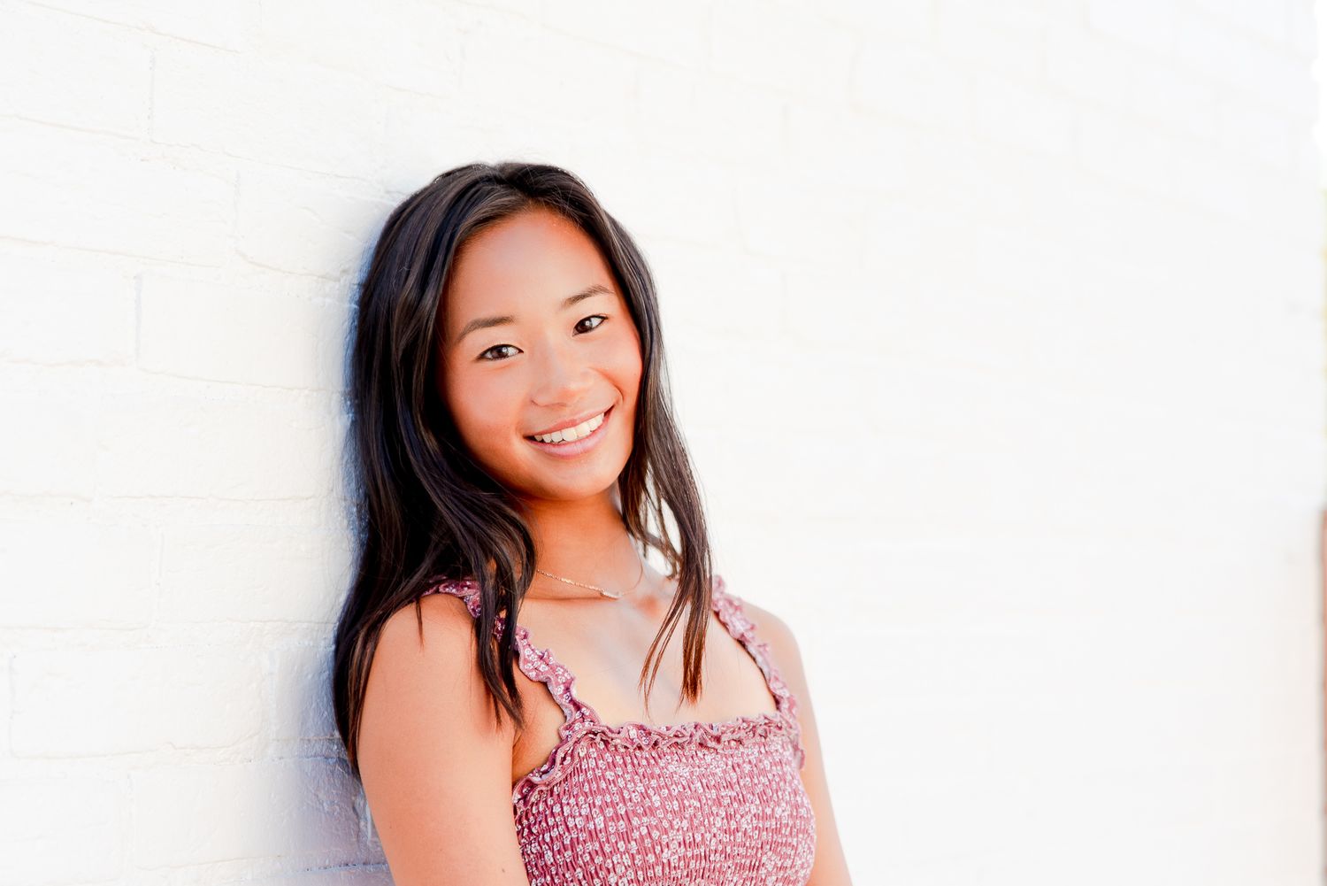girl in red dress leaning against white brick wall