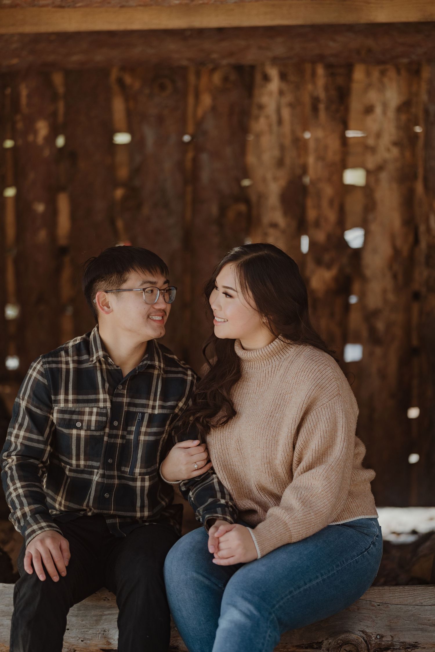 A couple shares an intimate moment while sitting on a wooden bench in casual winter attire.