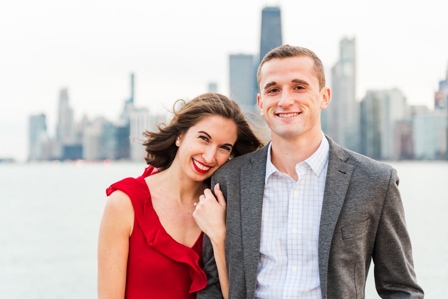 woman leaning on fiance shoulder, both smiling in front of Chicago skyline at North Ave Beach