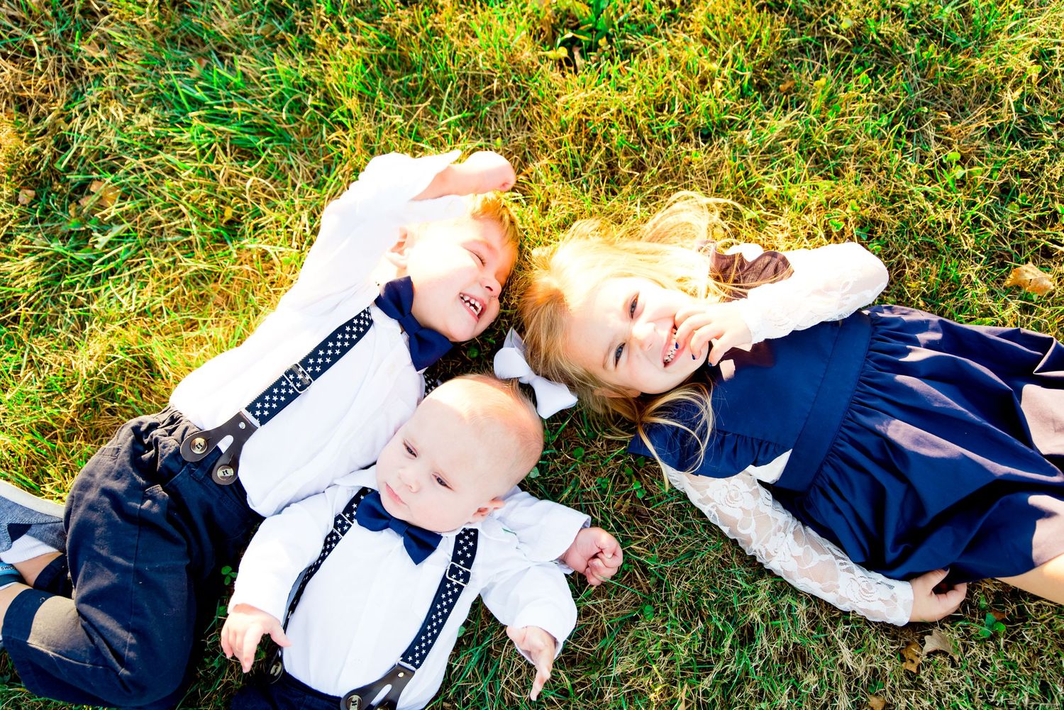 three young children in navy and white laying in the grass at Grant Park laughing at each other