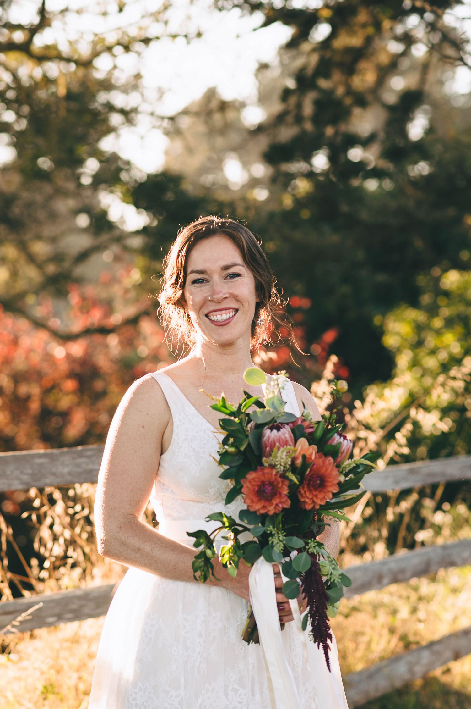 Beautiful bride in a golden grassy field with bouquet of red and orange flowers.