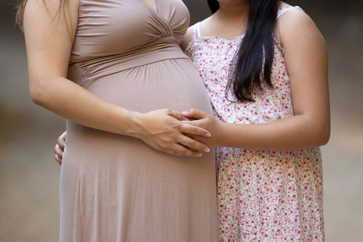 close up of mother's pregnant belly with daughter's hands on it