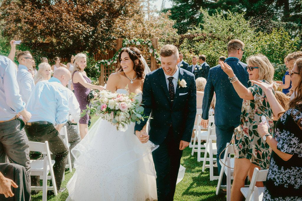 Outdoor garden wedding ceremony with guests seated on white chairs.