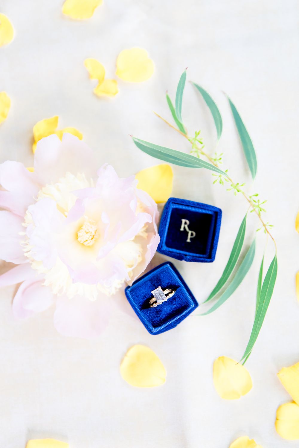 emerald cut diamond ring in blue box with RP next to peony, greenery, and yellow rose petals