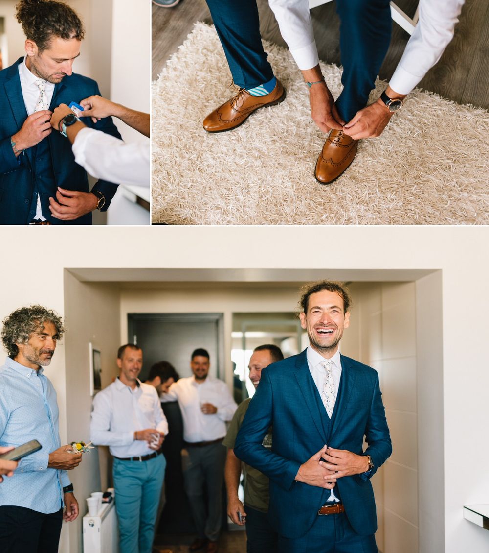 Groom wearing navy suit stands confidently while groomsmen prepare in background.