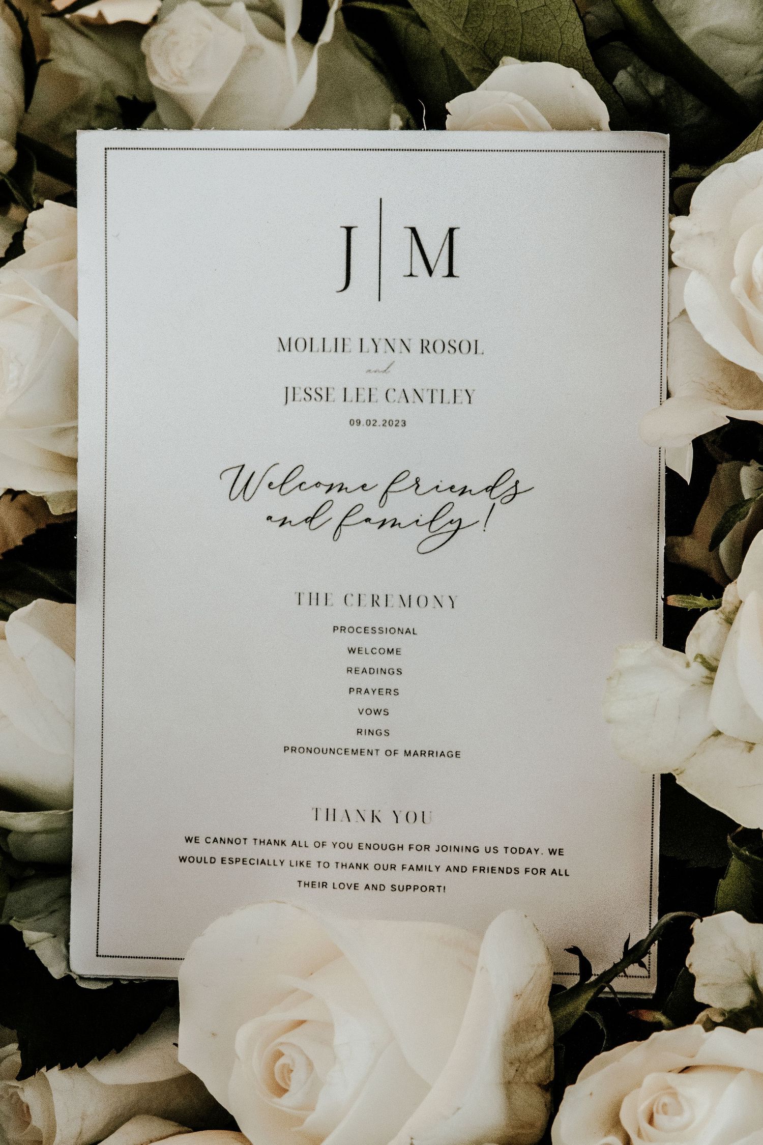 Wedding invitation with monogram design surrounded by white roses and greenery.
