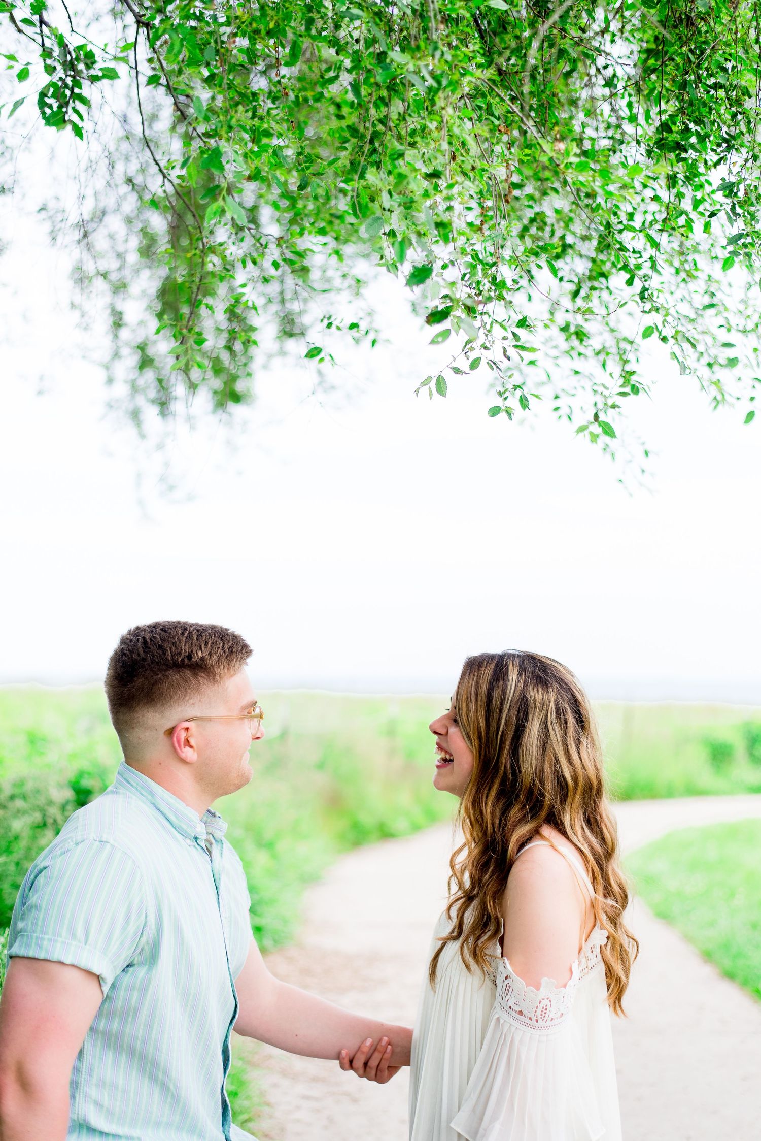 young couple in light blue and white laughing under a tree at Montrose Harbor sunrise engagement pictures