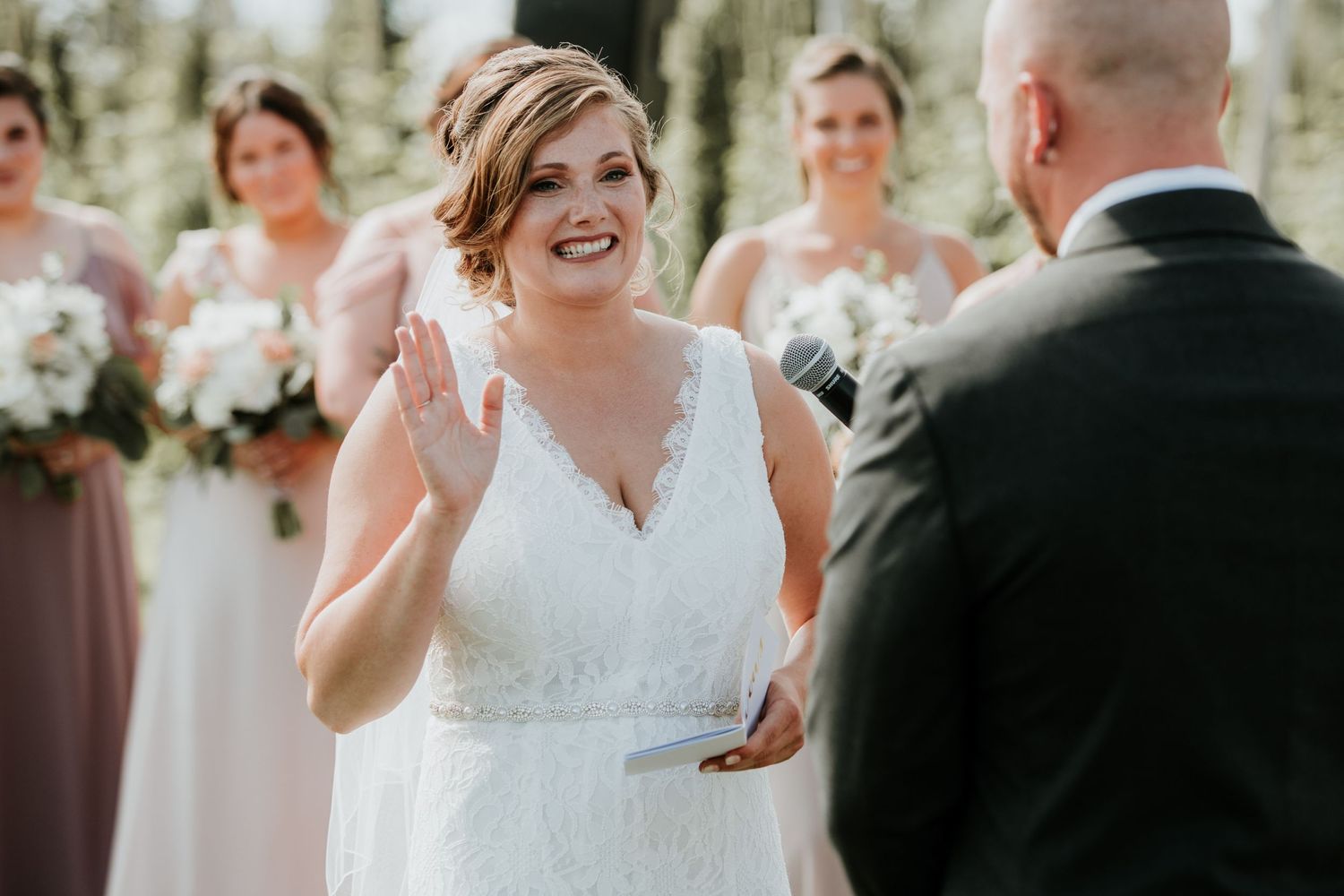 bride giving her vows with her hand raised high back of the groom is in the frame