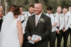 groom with groomsmen smiling behind him while he gives his vows