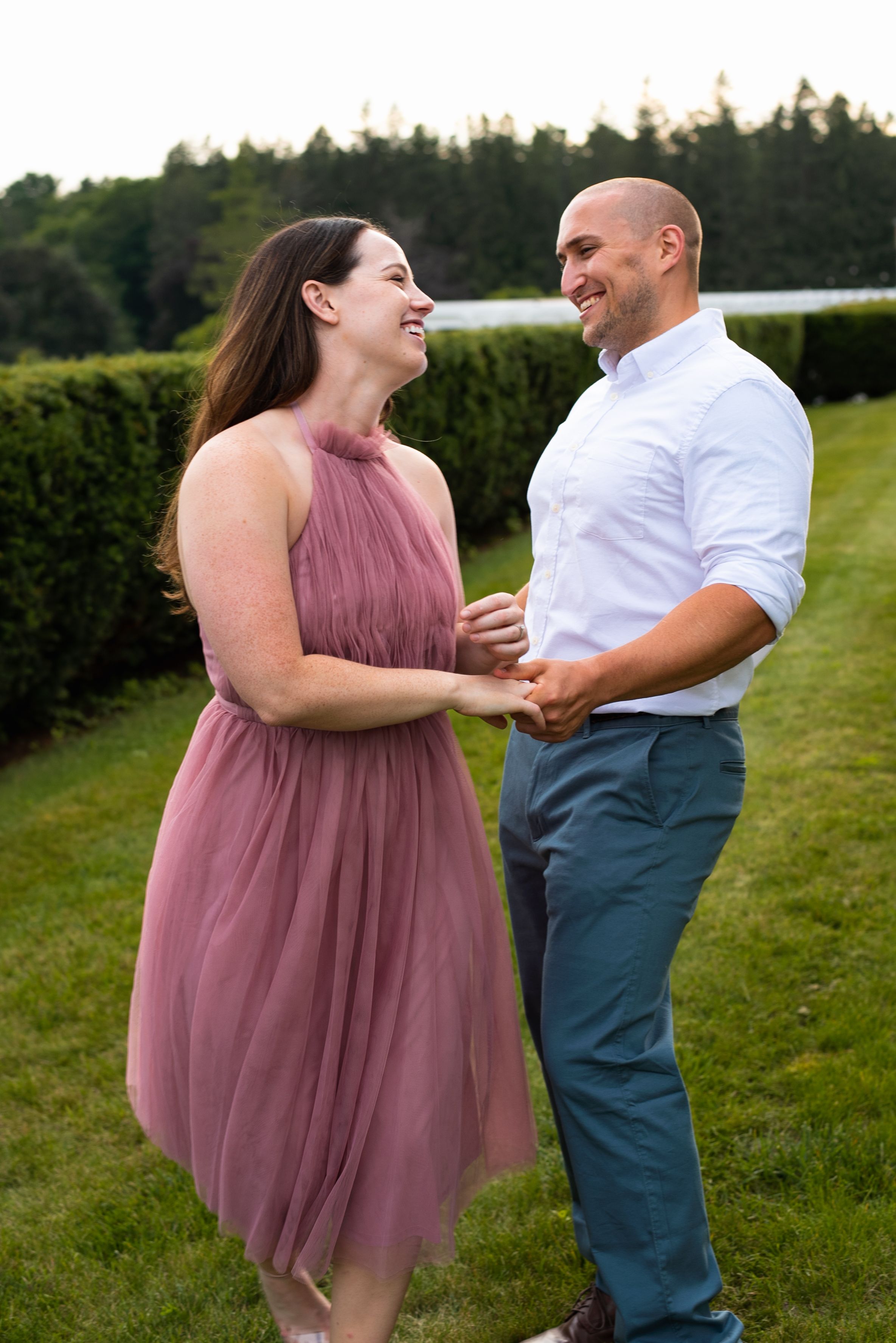 A couple shares a joyful moment together on a manicured lawn with hedges in the background.