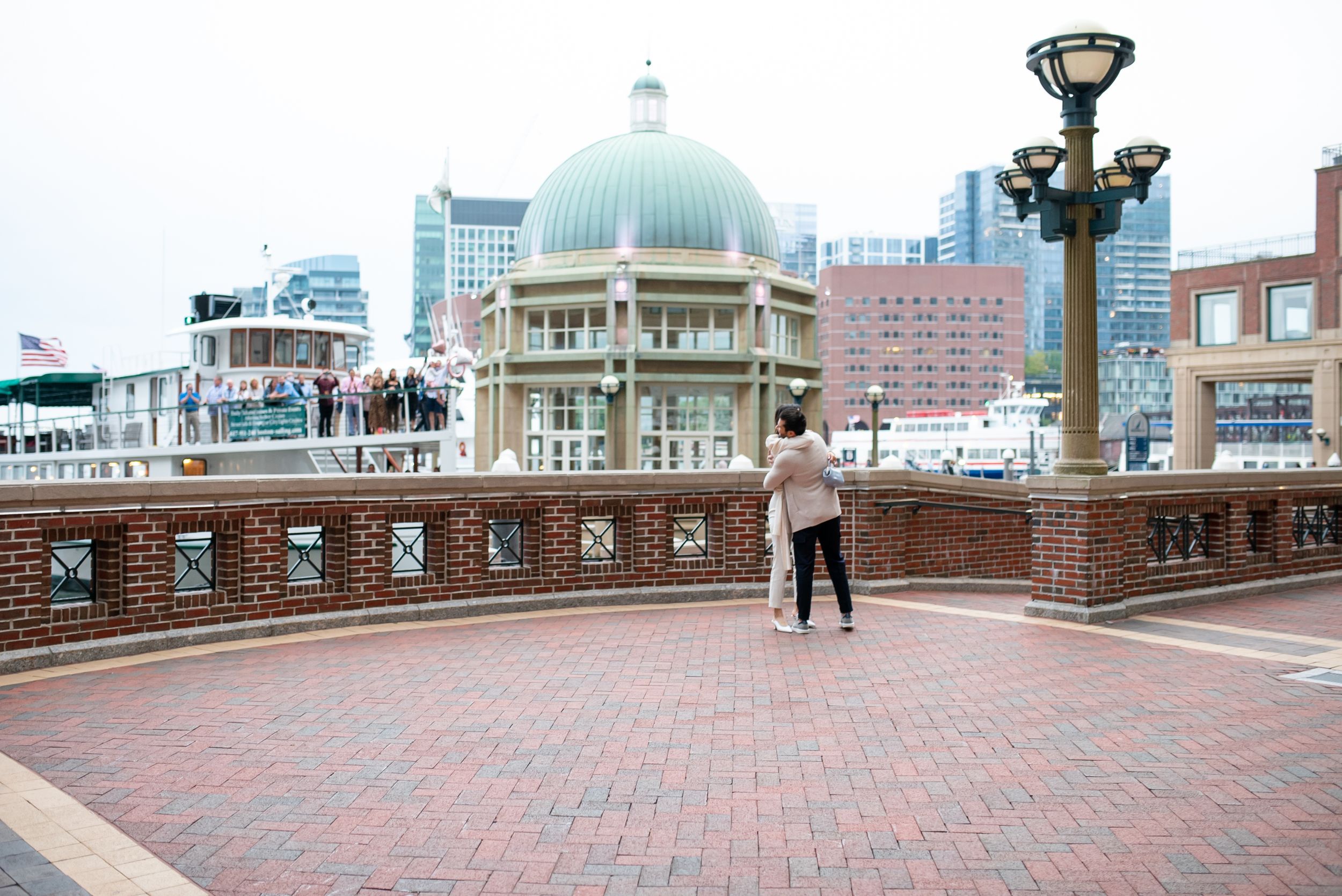 Urban waterfront scene with brick walkway and domed building in background.