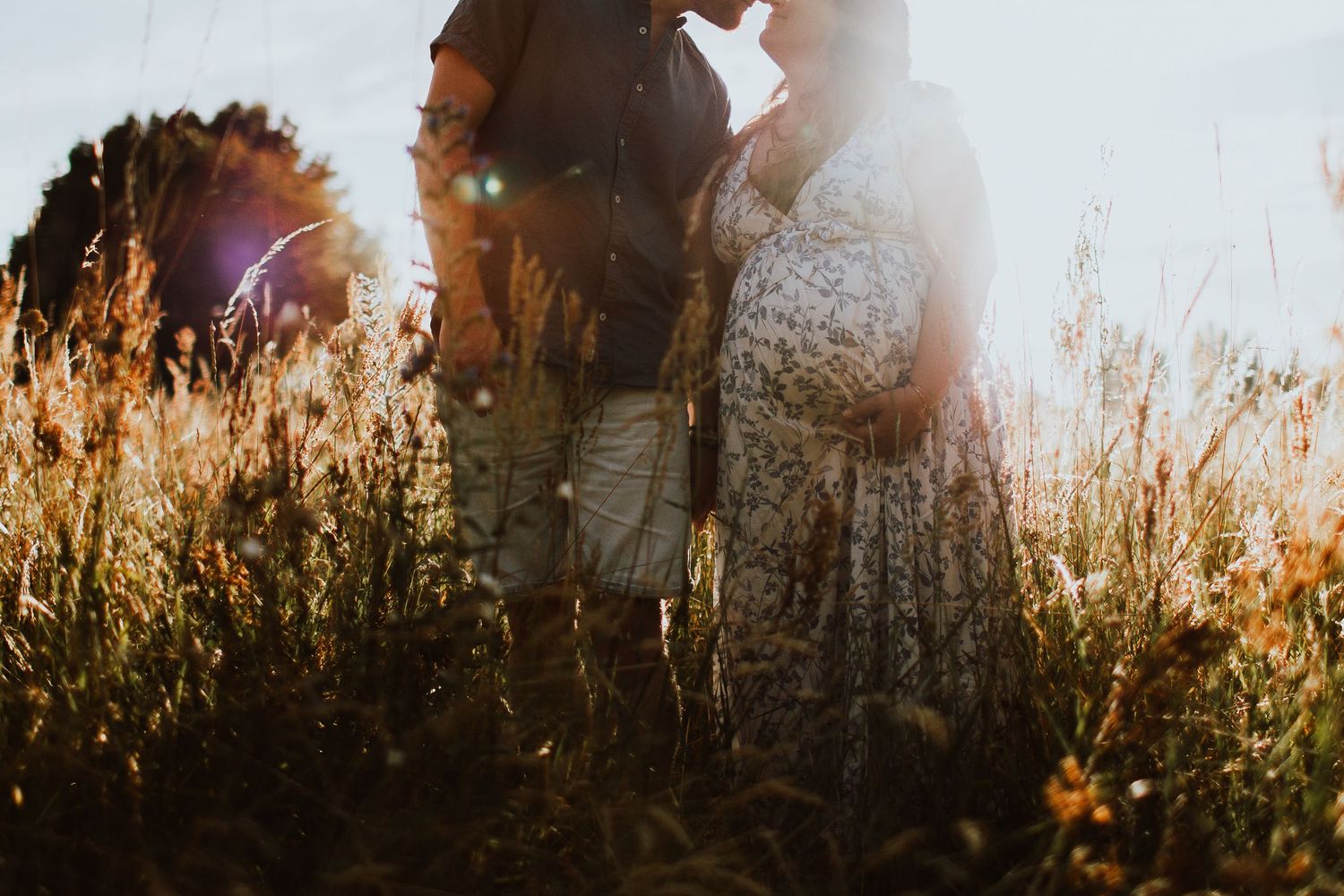 Dreamy backlit photo of couple standing in golden field at sunset.