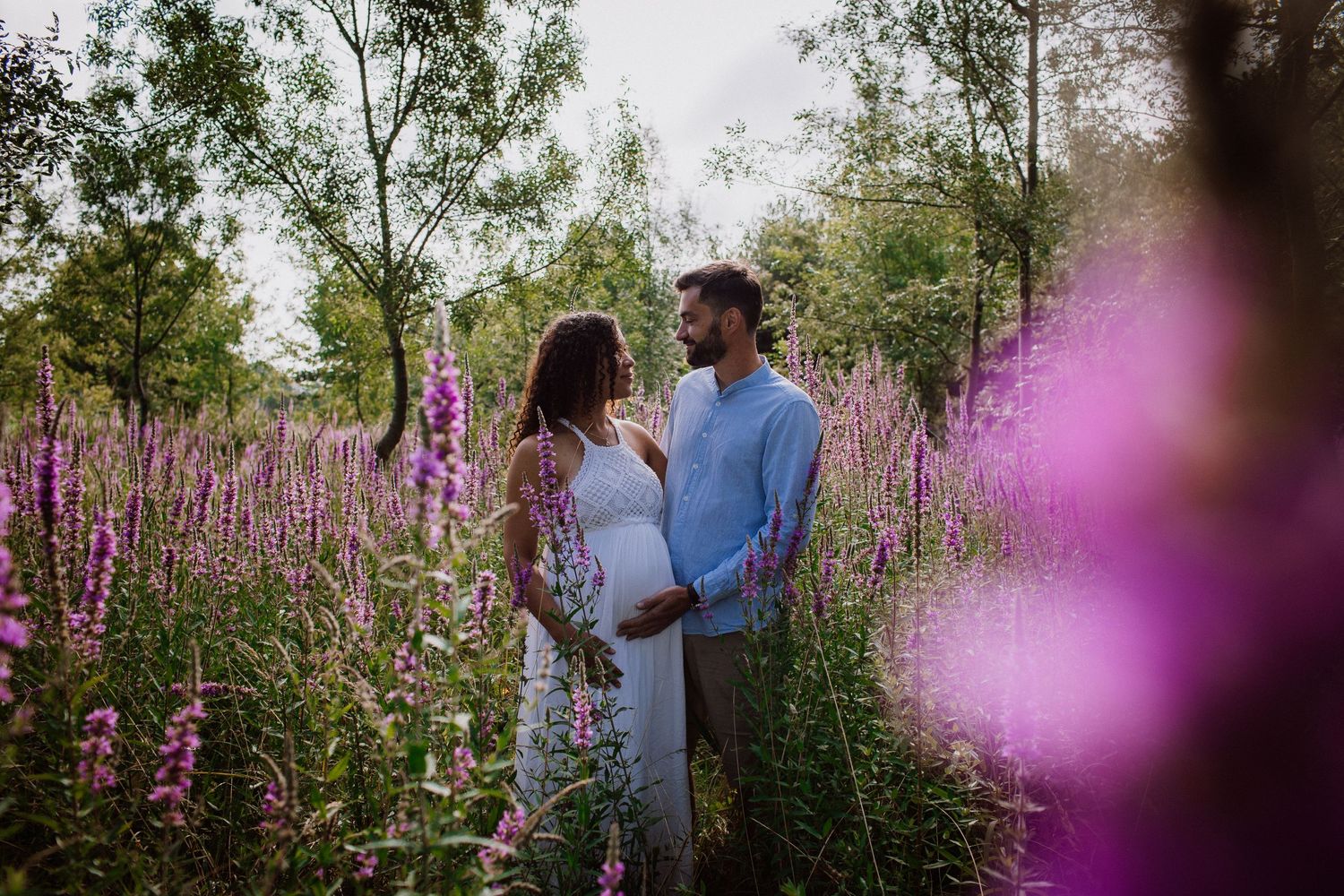 Expecting couple shares intimate moment among purple wildflowers in meadow.
