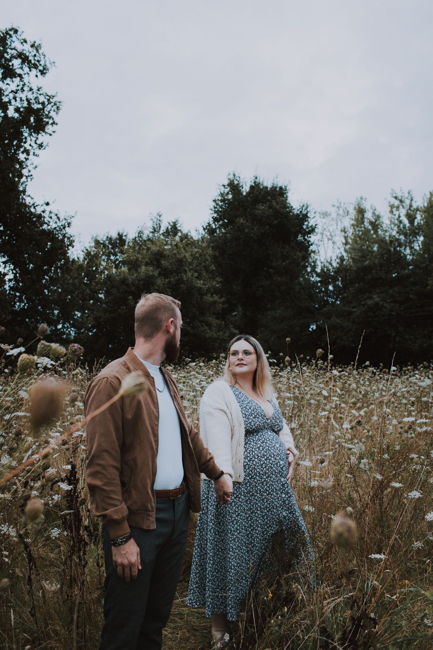 Couple standing together in a field of tall wildflowers at sunset.