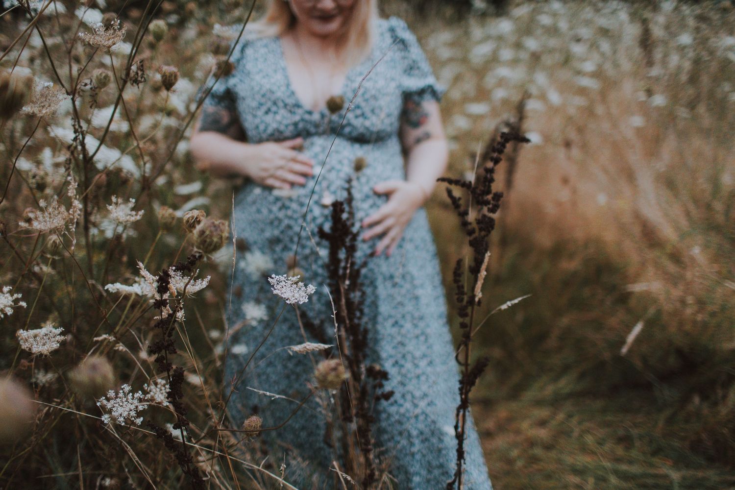Person in a floral dress standing among wild grasses and flowers.