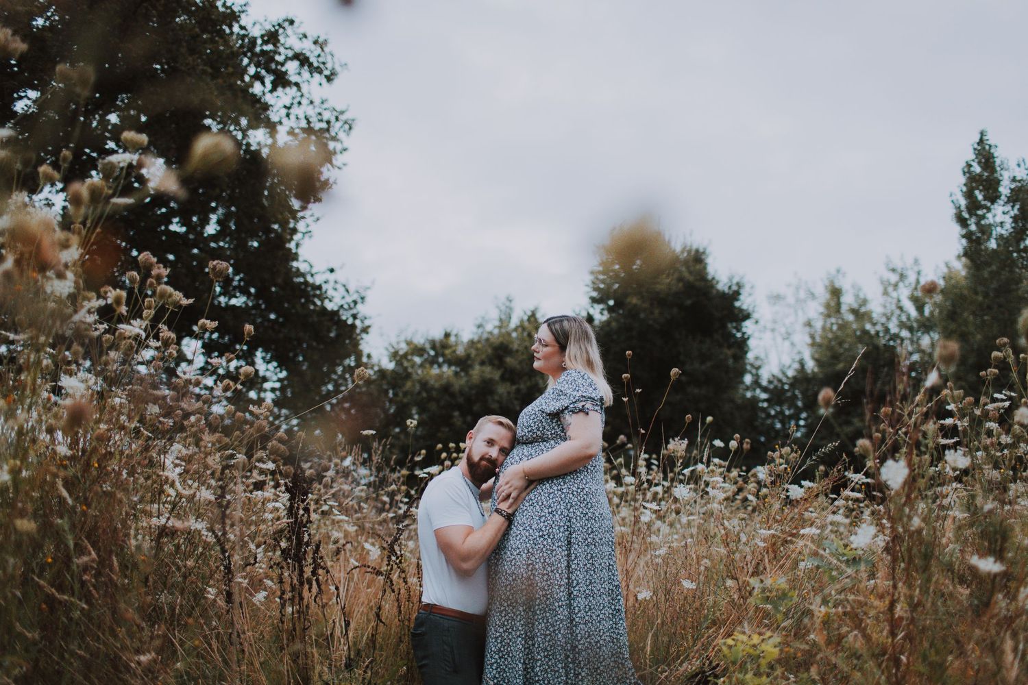 Expecting couple embracing in a field of dried wildflowers.