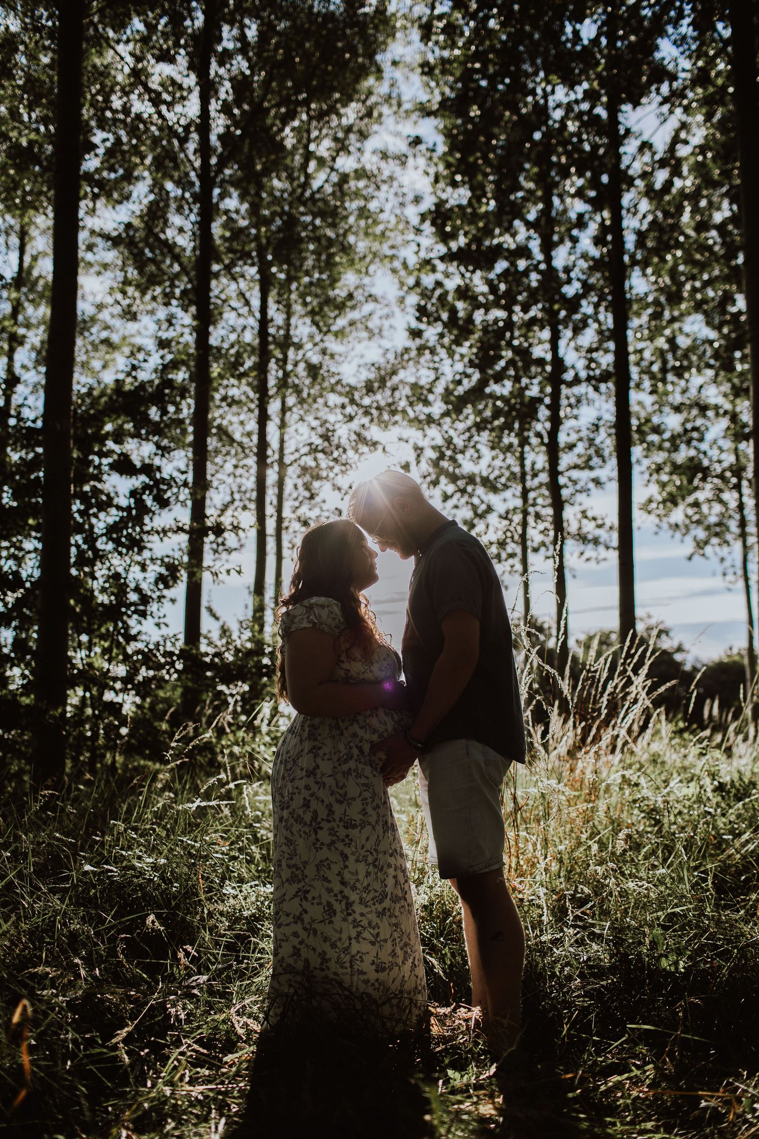 Romantic silhouette of couple embracing in sunlit forest with tall trees.