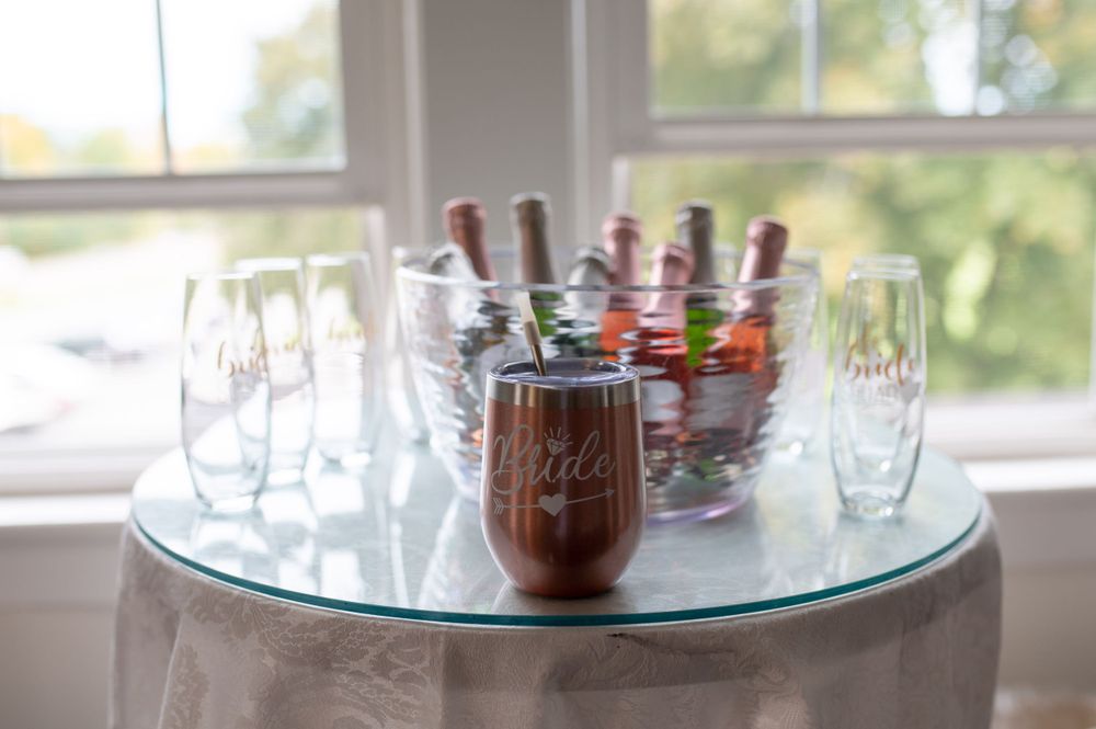 Wedding reception drinks setup with wine glasses and custom tumblers on a round table.