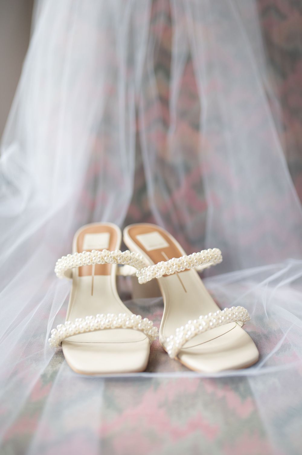 Pearl-embellished bridal sandals displayed with delicate white tulle veil.