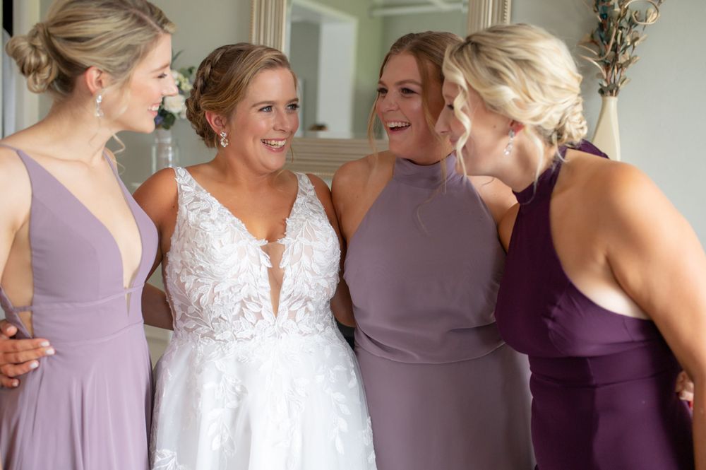 Bridesmaids in purple dresses share a joyful moment during wedding preparations.