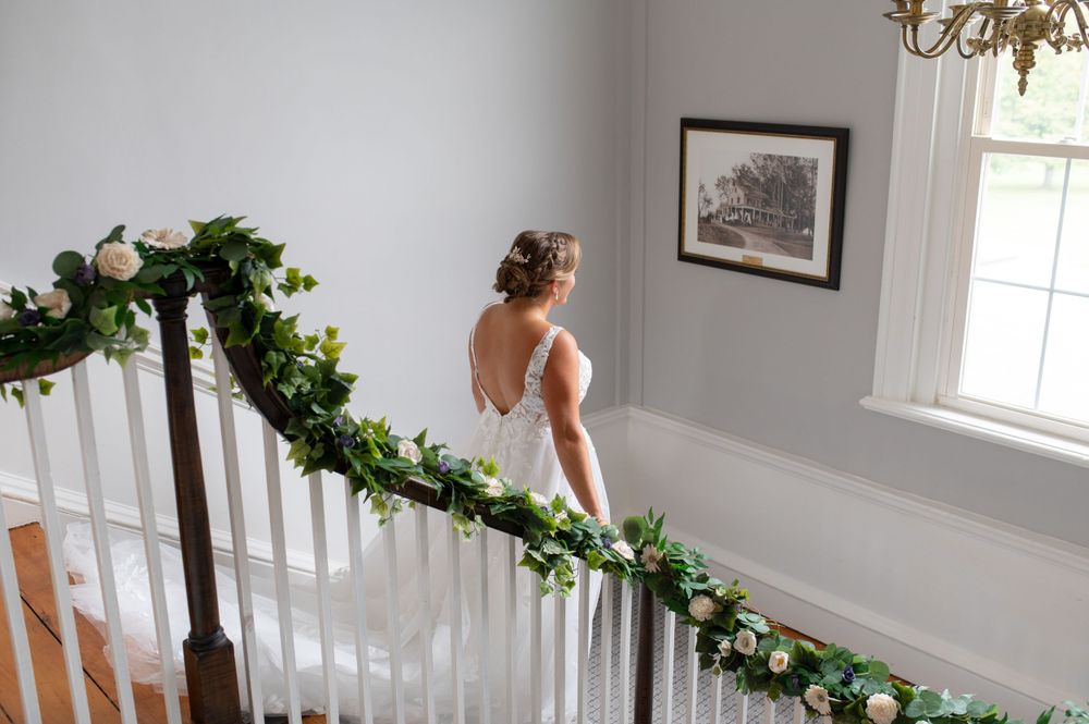 Wedding dress trailing down a white staircase decorated with greenery and lights.