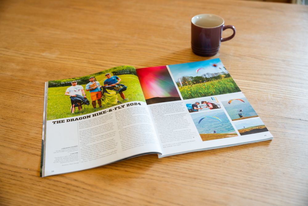 Open magazine with colorful photos displayed on wooden table next to purple coffee mug.
