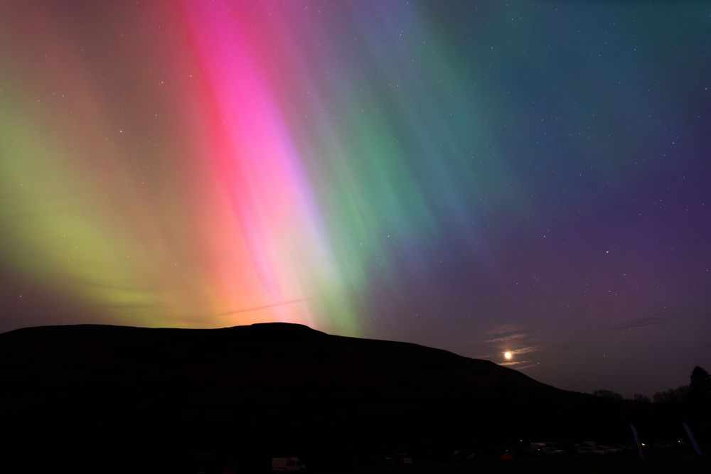 Vibrant aurora borealis displays pink and green lights across dark night sky.