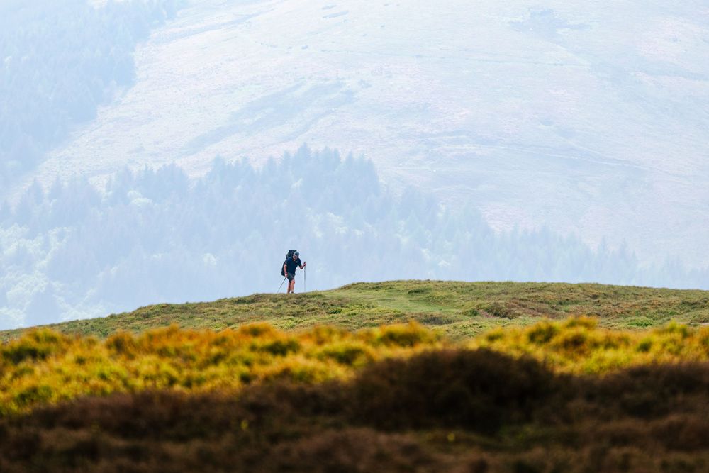 Silhouette of person standing on hilltop overlooking mountainous landscape.