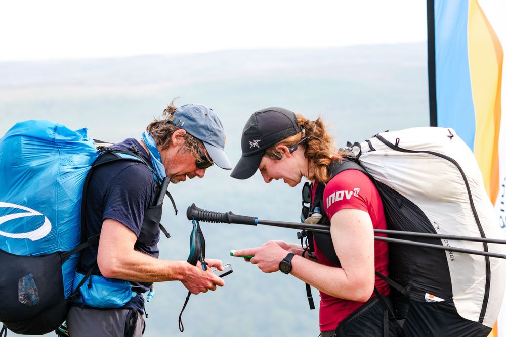 Two people examining paragliding equipment with backpacks and gear.