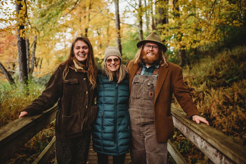 Three people standing together on wooden bridge during autumn season.