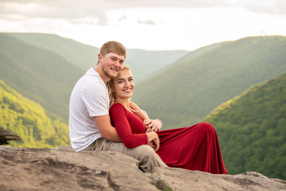 Couple sharing a romantic moment on a mountain overlook with scenic valley views in the background.