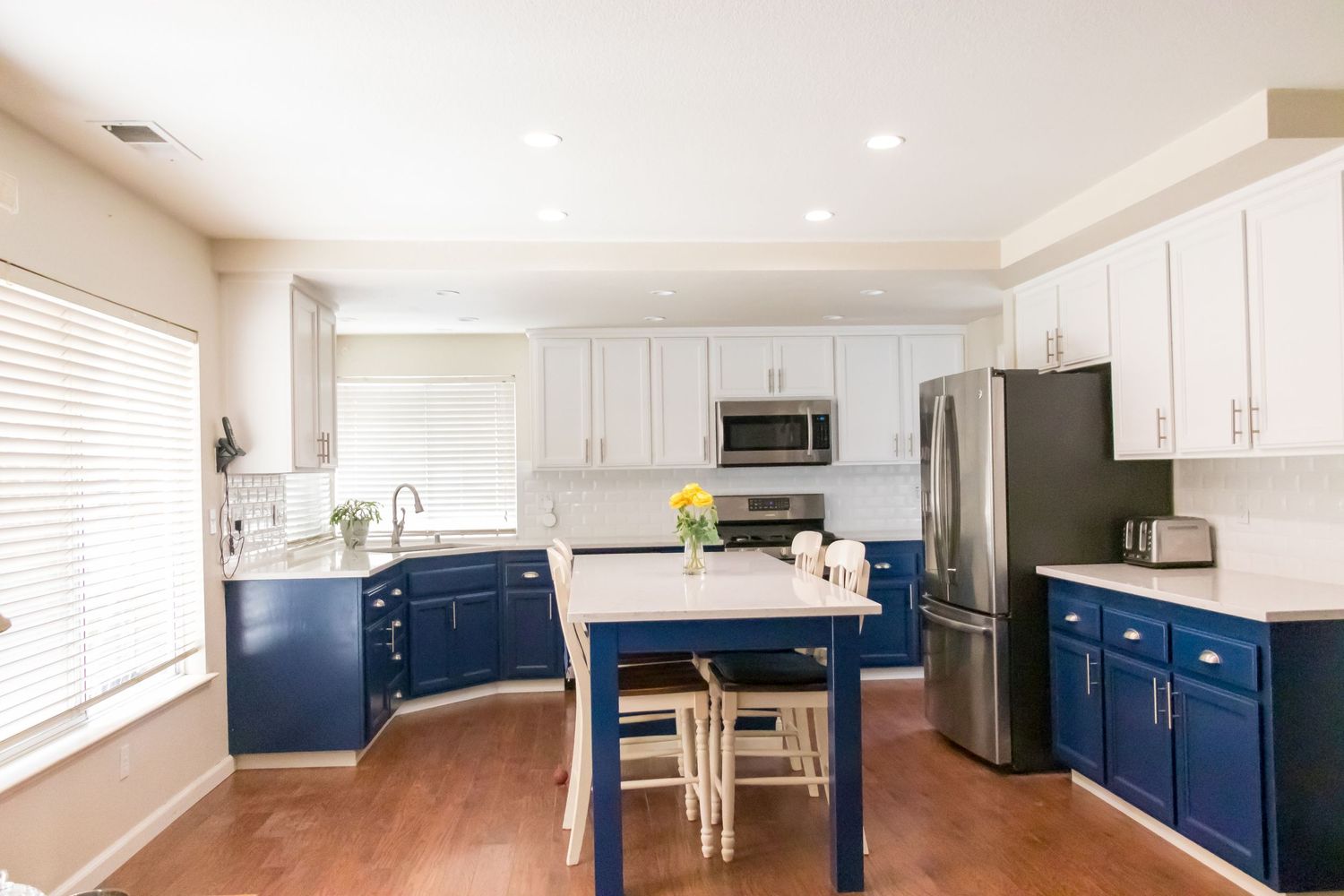 Modern kitchen with white upper cabinets, navy blue lower cabinets, and stainless steel appliances.