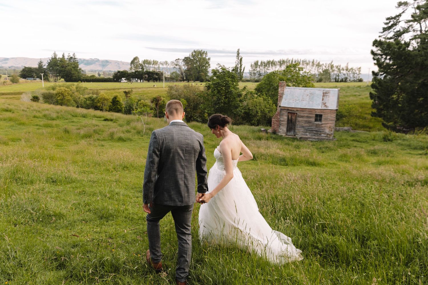 A romantic wedding photo overlooking a rustic countryside with a small stone building in the distance.