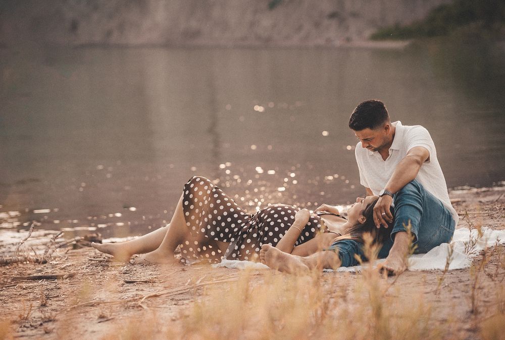 A couple relaxes on a picnic blanket by a tranquil lake, enjoying a romantic afternoon together.