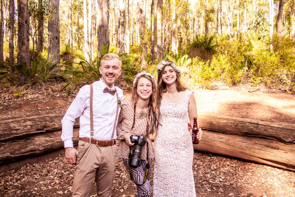 A casual wedding photo in a sunlit forest with rustic attire and natural scenery.
