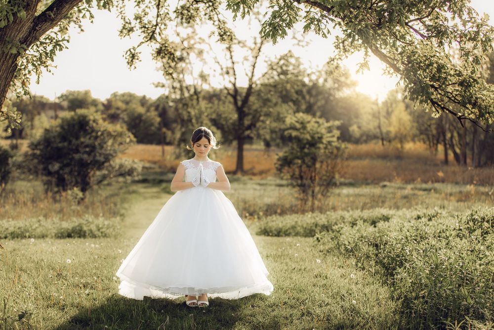 A flowing white wedding gown shimmers in golden sunlight amid a serene garden setting at sunset.