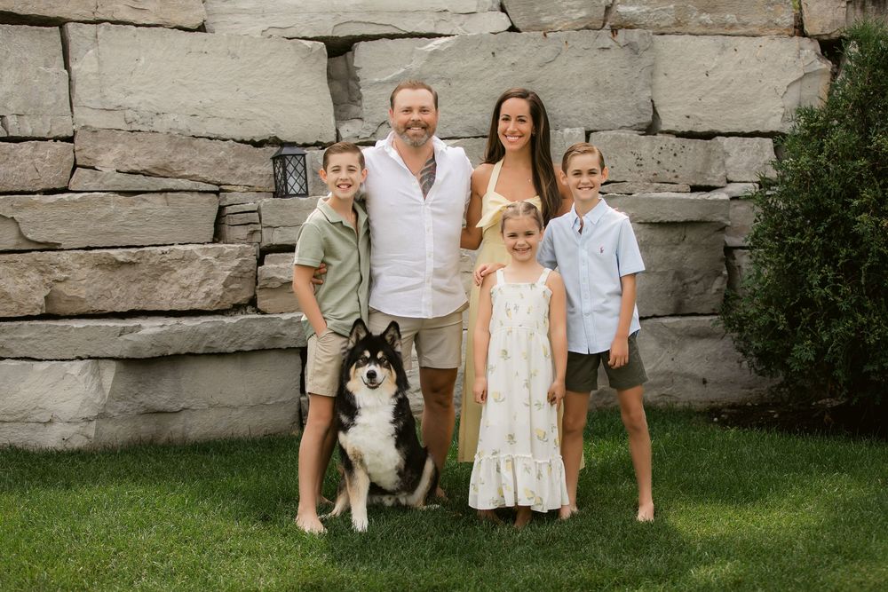 A family sits together on a stone wall with their large Husky dog at sunset.