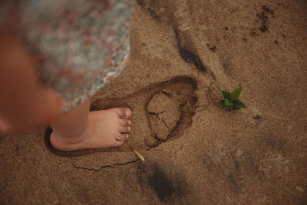 Close up of small bare feet on sandy beach with heart drawn in sand.