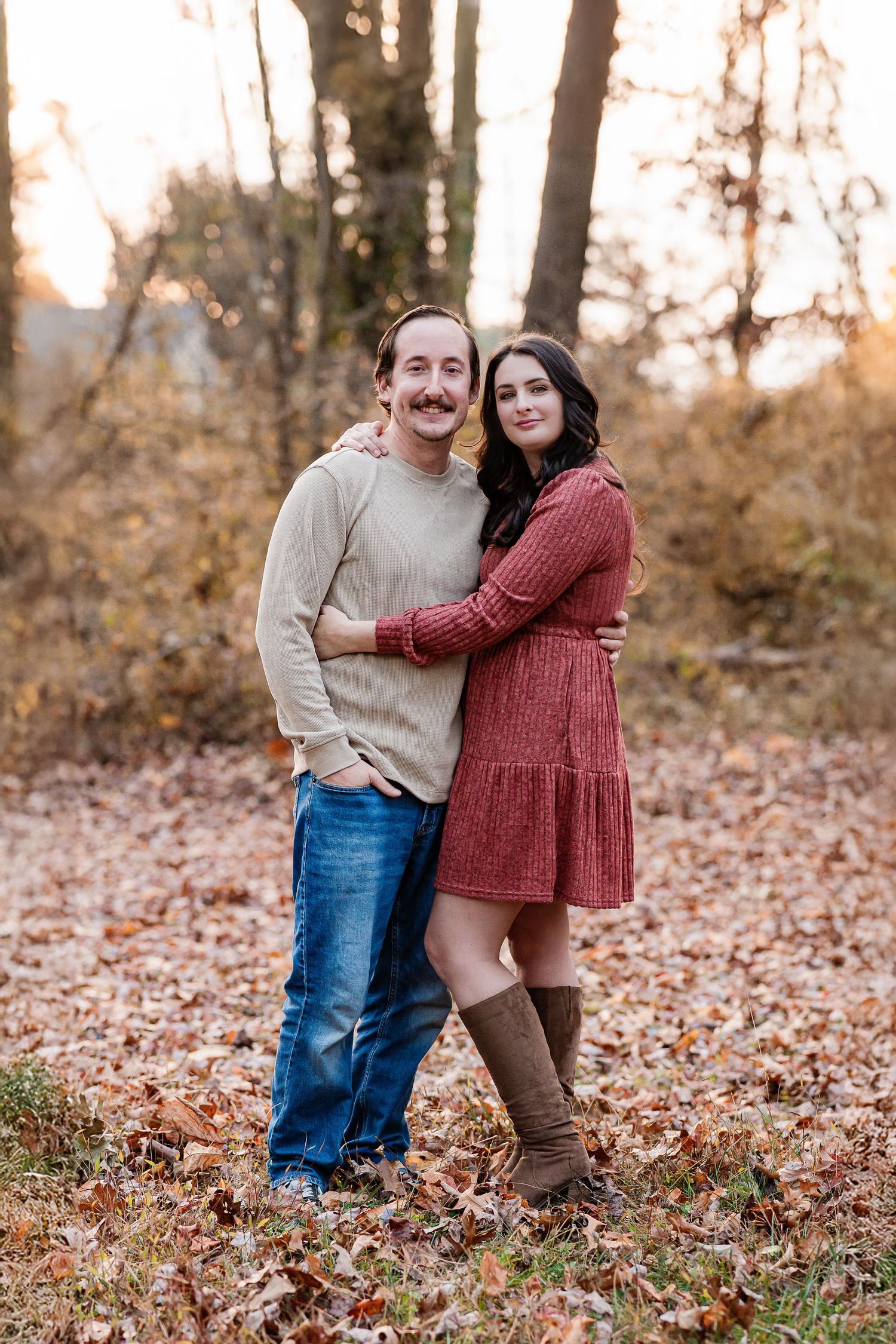 A couple poses together in autumn foliage wearing casual fall outfits.