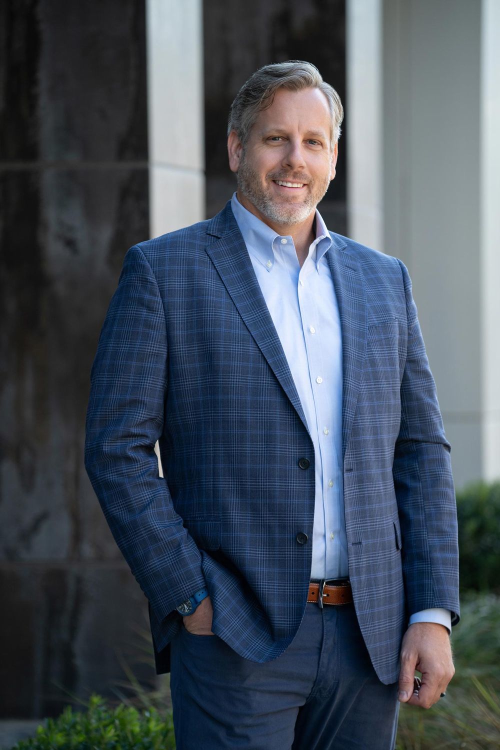 Professional portrait of someone in a blue plaid blazer standing against white columns.