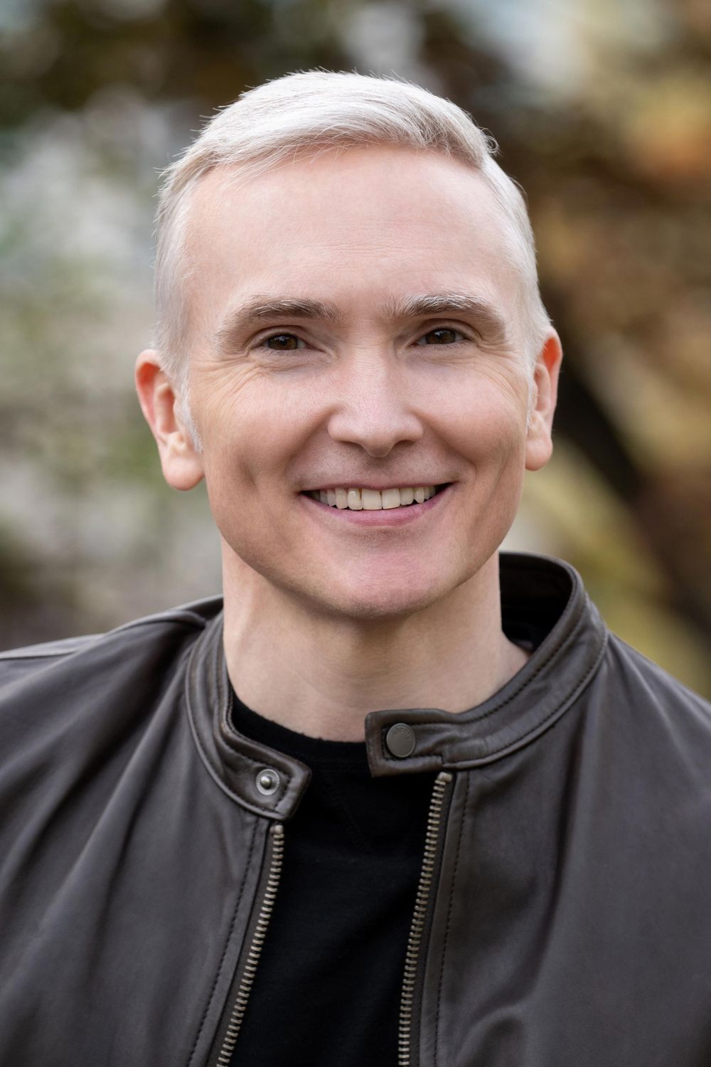 Professional headshot of a person with short grey hair wearing a dark jacket and smiling at the camera.