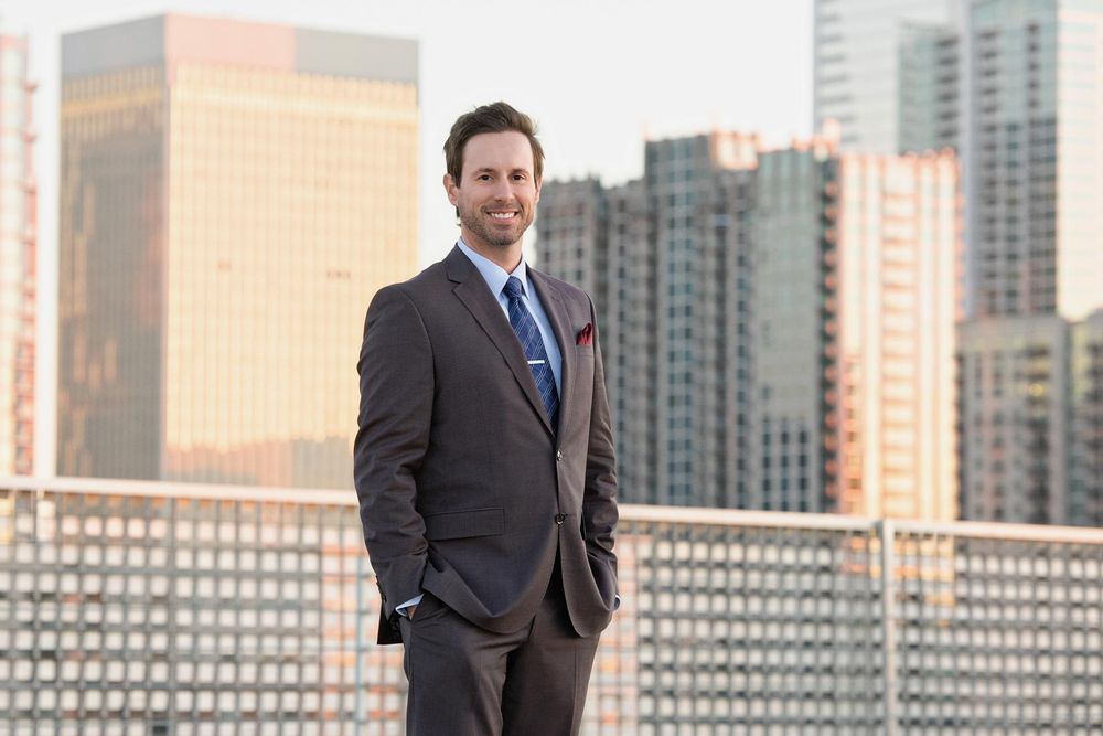 Business professionals stand on urban rooftop with modern city skyline in background during sunny day.