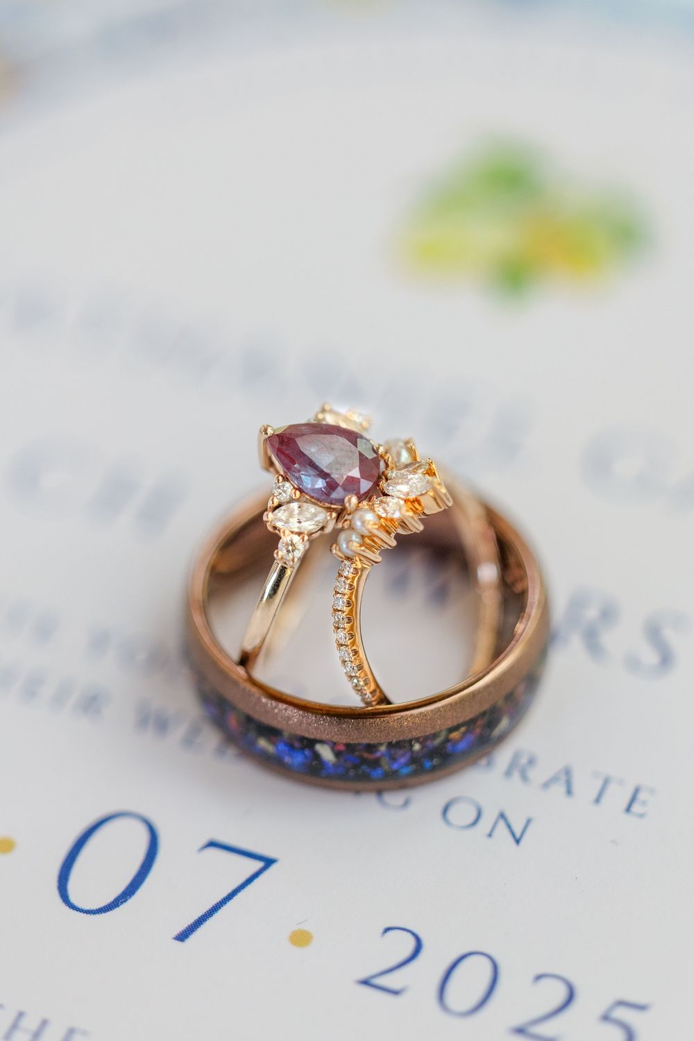 Wedding rings photographed on a calendar showing a 2025 date, featuring a purple gemstone engagement ring and blue inlaid band.
