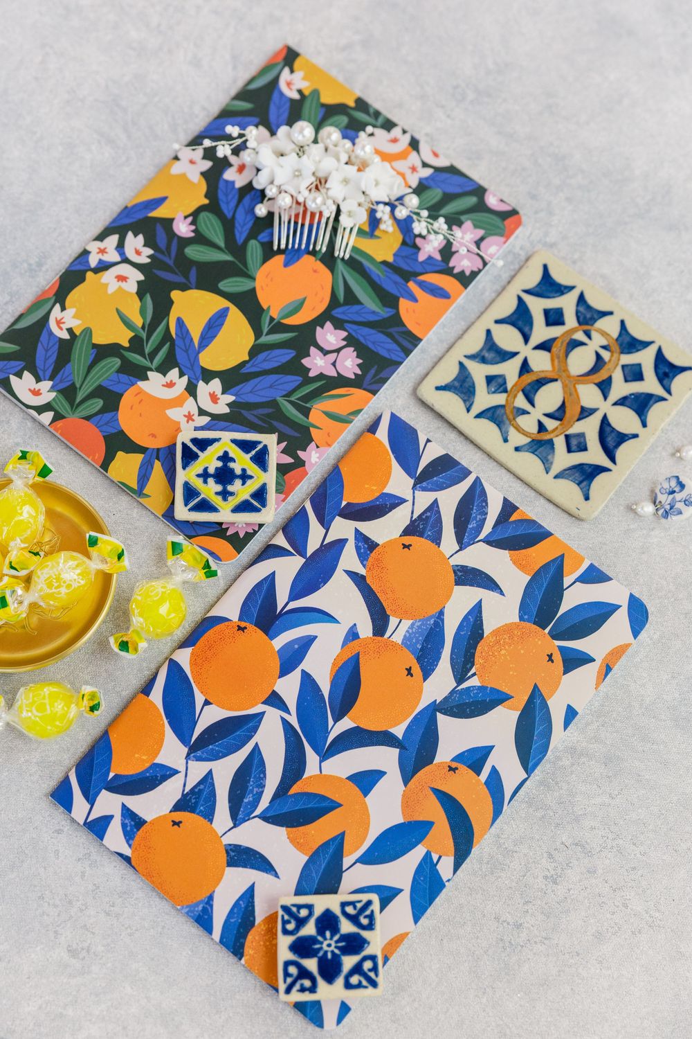 Colorful floral and citrus patterned fabric pouches with blue geometric tile designs and yellow candies beside them.