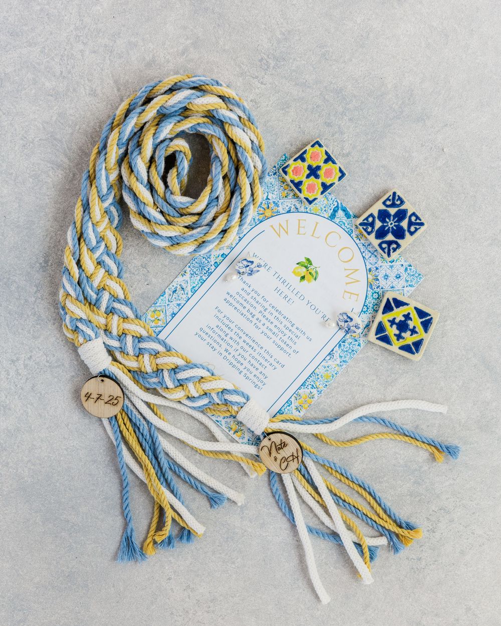 Decorative blue and gold braided cord with tassels and ornate tiles arranged alongside a white invitation card.