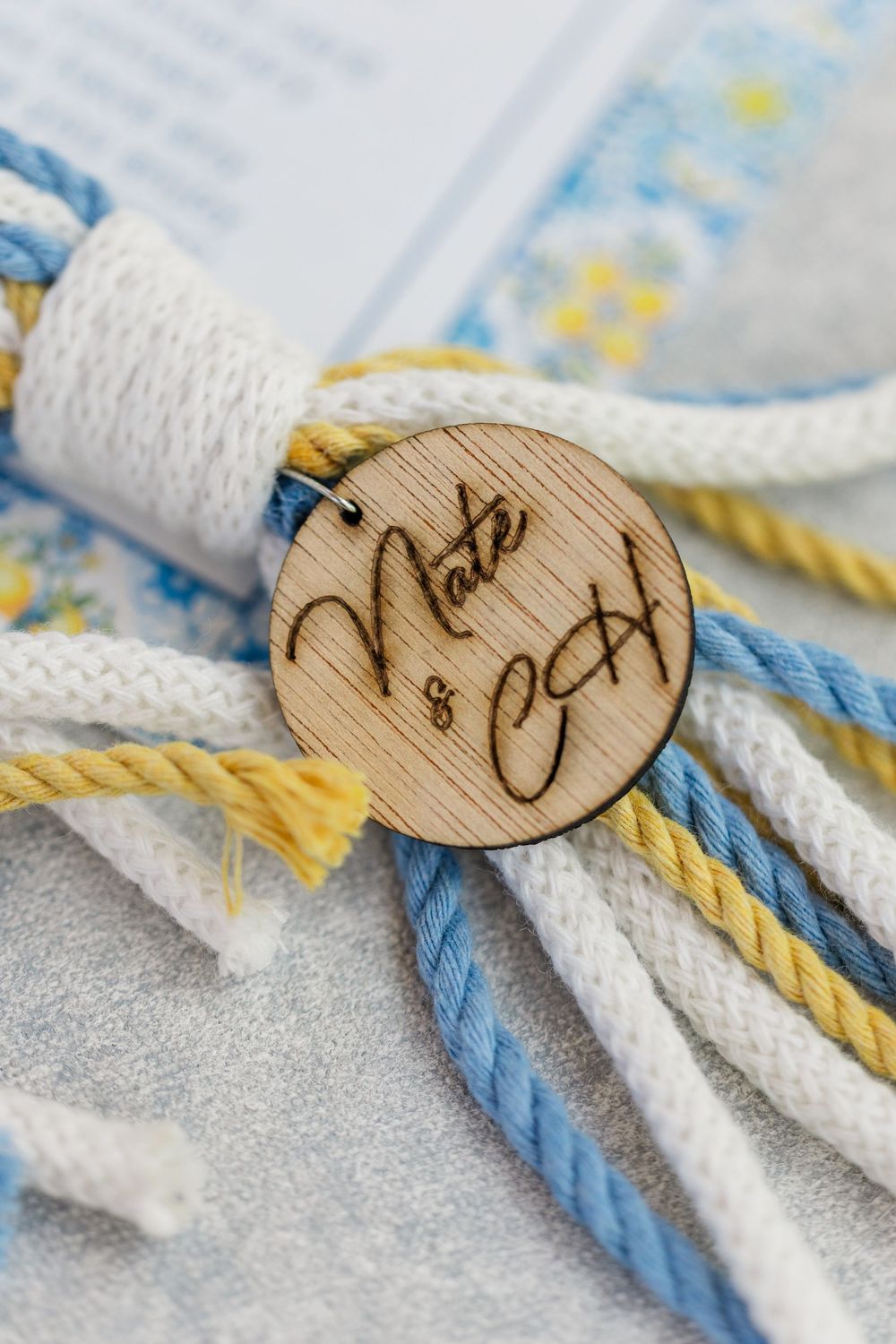 Close-up of a wooden button with text engraving attached to white and blue decorative ropes.