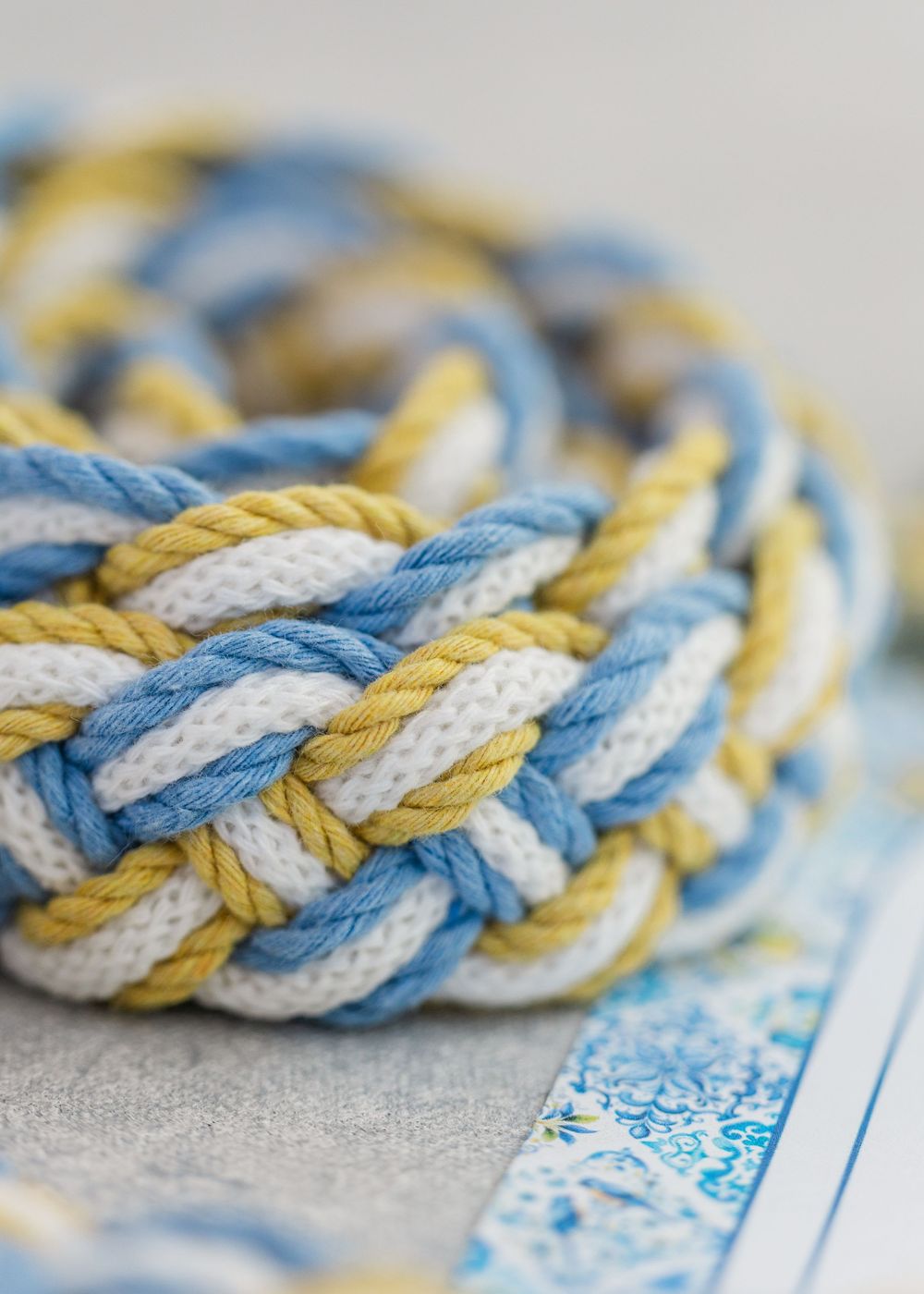 Close-up detail of braided twisted rope pattern in blue, yellow and white colors against linen background.