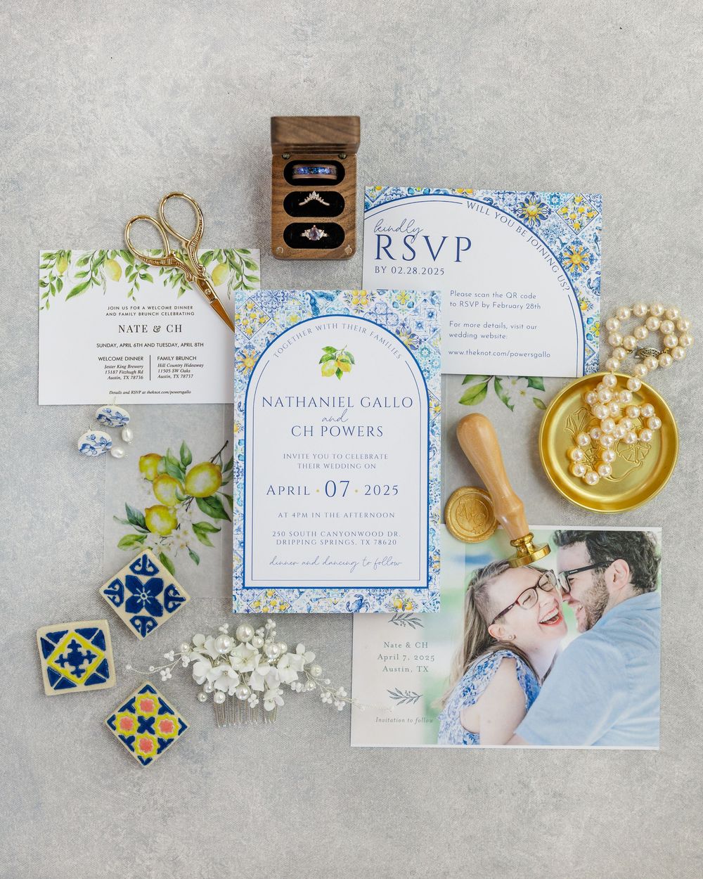 Wedding invitation suite in blue and white floral design with decorative tiles and golden scissors on gray surface.