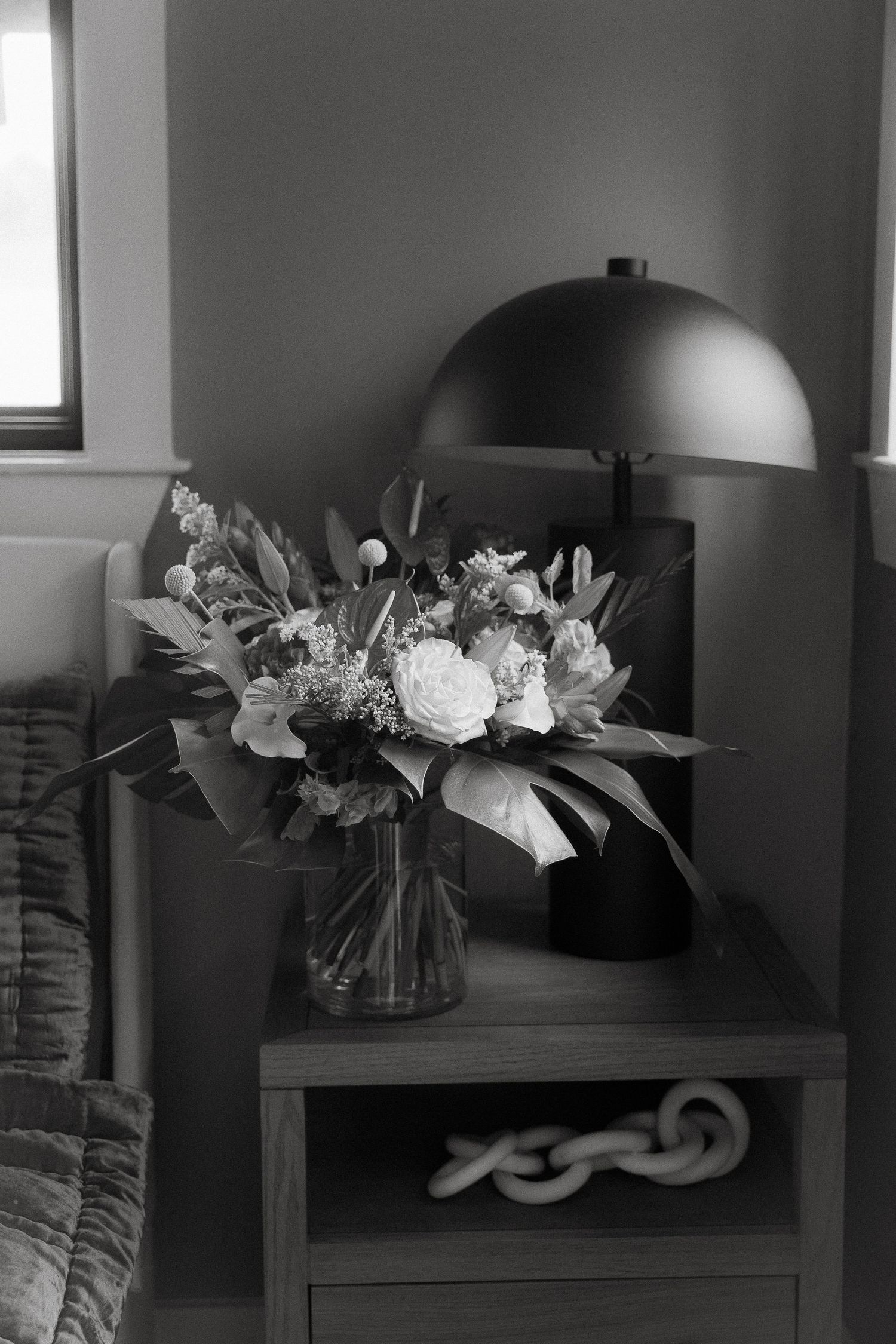 Black and white photograph of a floral arrangement in a glass vase on a side table with a modern dome lamp.